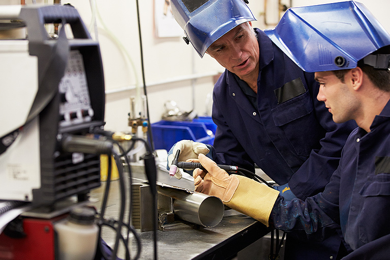 Welder helping apprentice in the studio