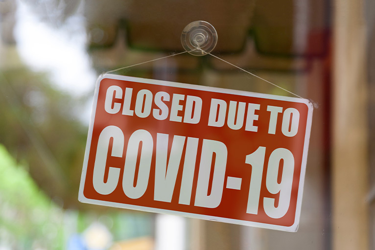 Red closed sign on business door, reading "Closed due to COVID-19"