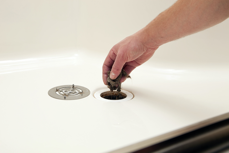 Plumbing problems: Hand pulling out hair and debris from shower