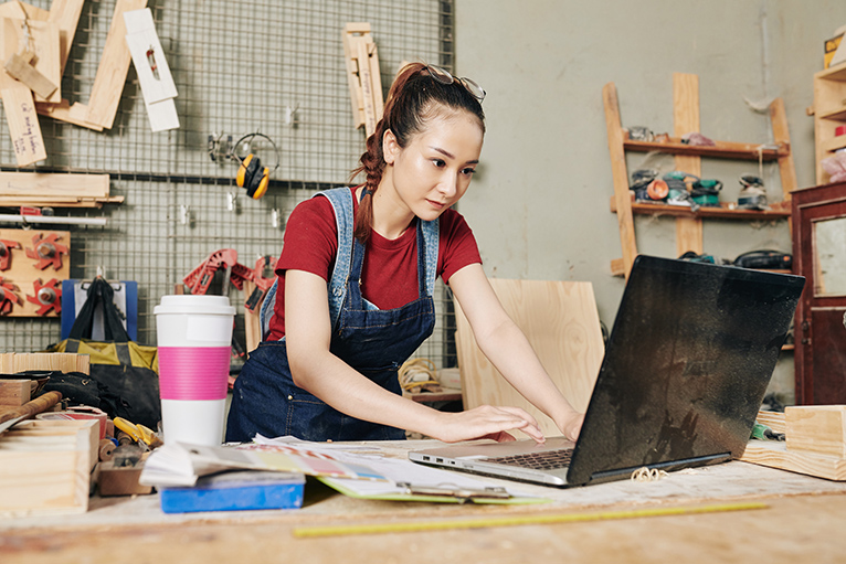 Trades training: Carpenter looking at laptop in workshop