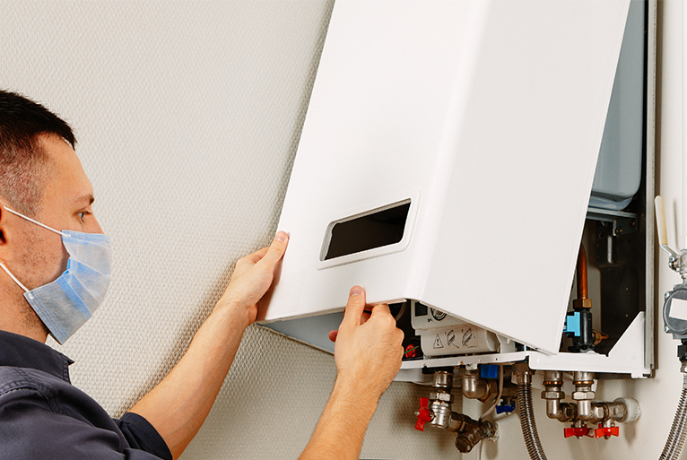 Energy efficiency home grants: Gas/heating engineer repairing boiler whilst wearing mask during the coronavirus pandemic