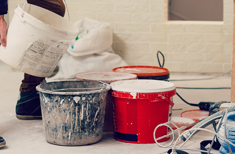 Large paint-splattered buckets, being filled with mist coat paint. 