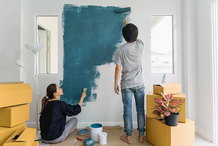 Young couple painting a wall blue together inside their new home. 