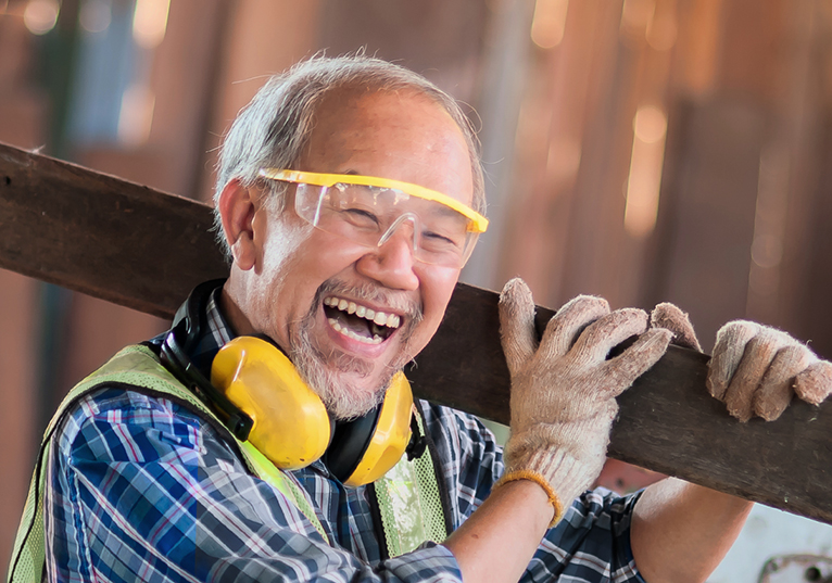 Smiling tradesman wearing his work uniform, carrying a plank of wood.