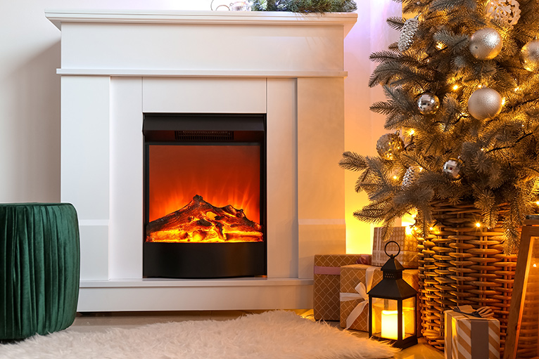 Switched-on electric fireplace with a Christmas tree and lantern beside it. 