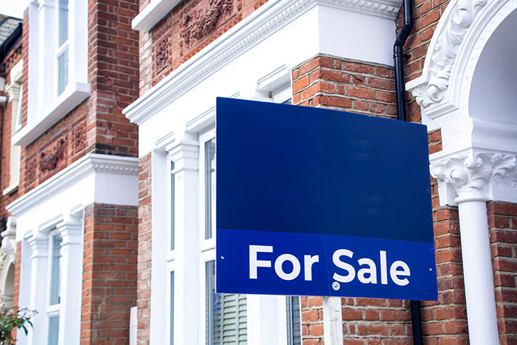 Estate agent 'For Sale' sign board with brick houses in background