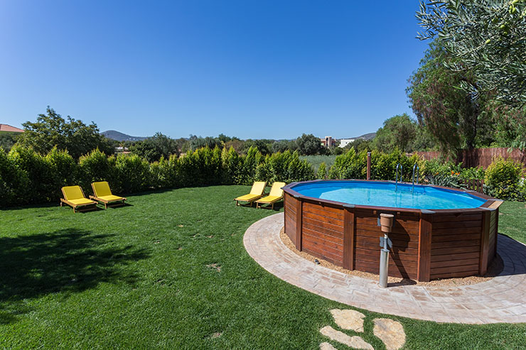 Image of an above ground pool placed on a concrete pad, in a garden, surrounded by grass and deck chairs