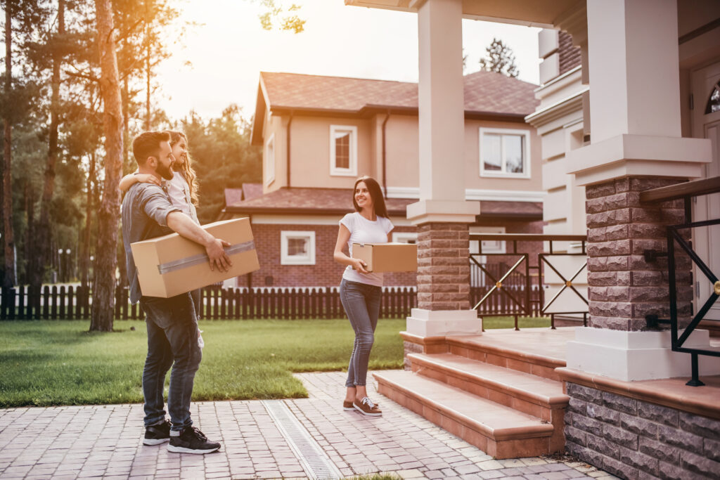 Picture of a couple standing in front of a house holding boxes with a small child in father's arms 