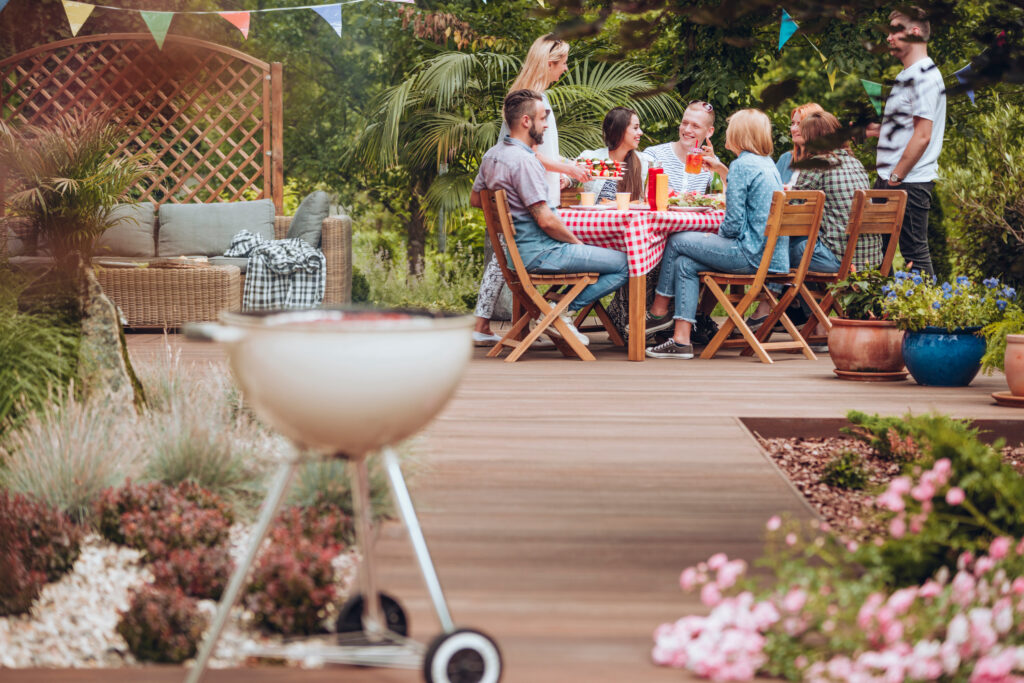 Picture of a garden with BBQ in forefront and table of people sitting towards the back